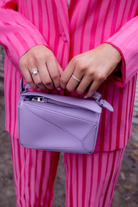 Loewe Mini Puzzle in Lilac being held by a woman wearing a pink stripe suit 